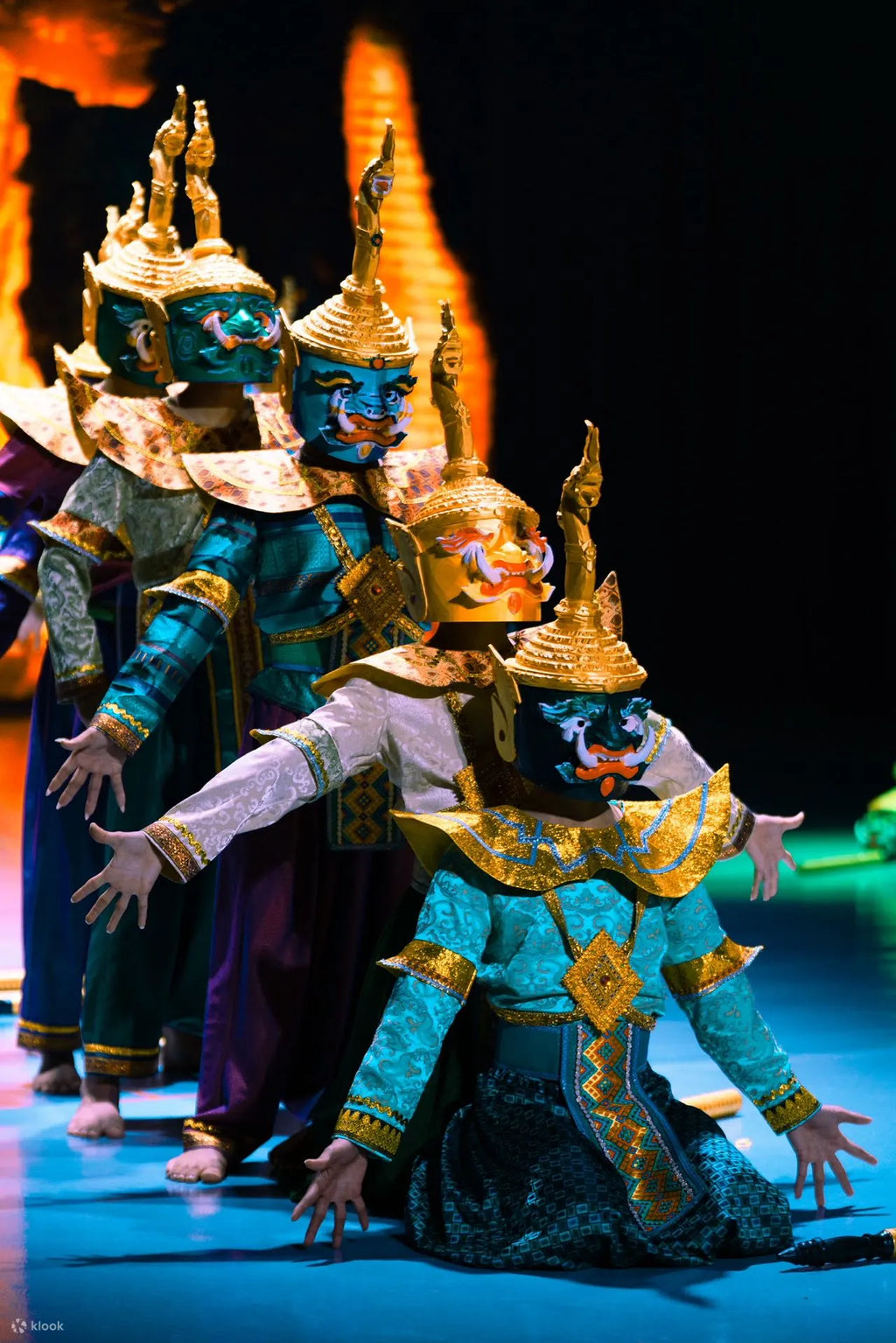Dancers in elaborate traditional costumes with gold headpieces on a stage.